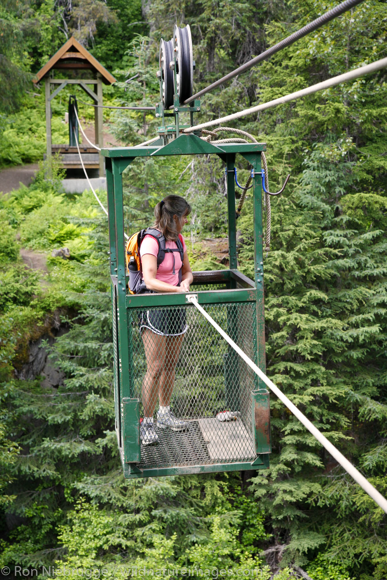 A hiker pulls herself across Glacier Creek on the aerial hand tram, Winner Creek Gorge Trail, Girdwood, Chugach National Forest...